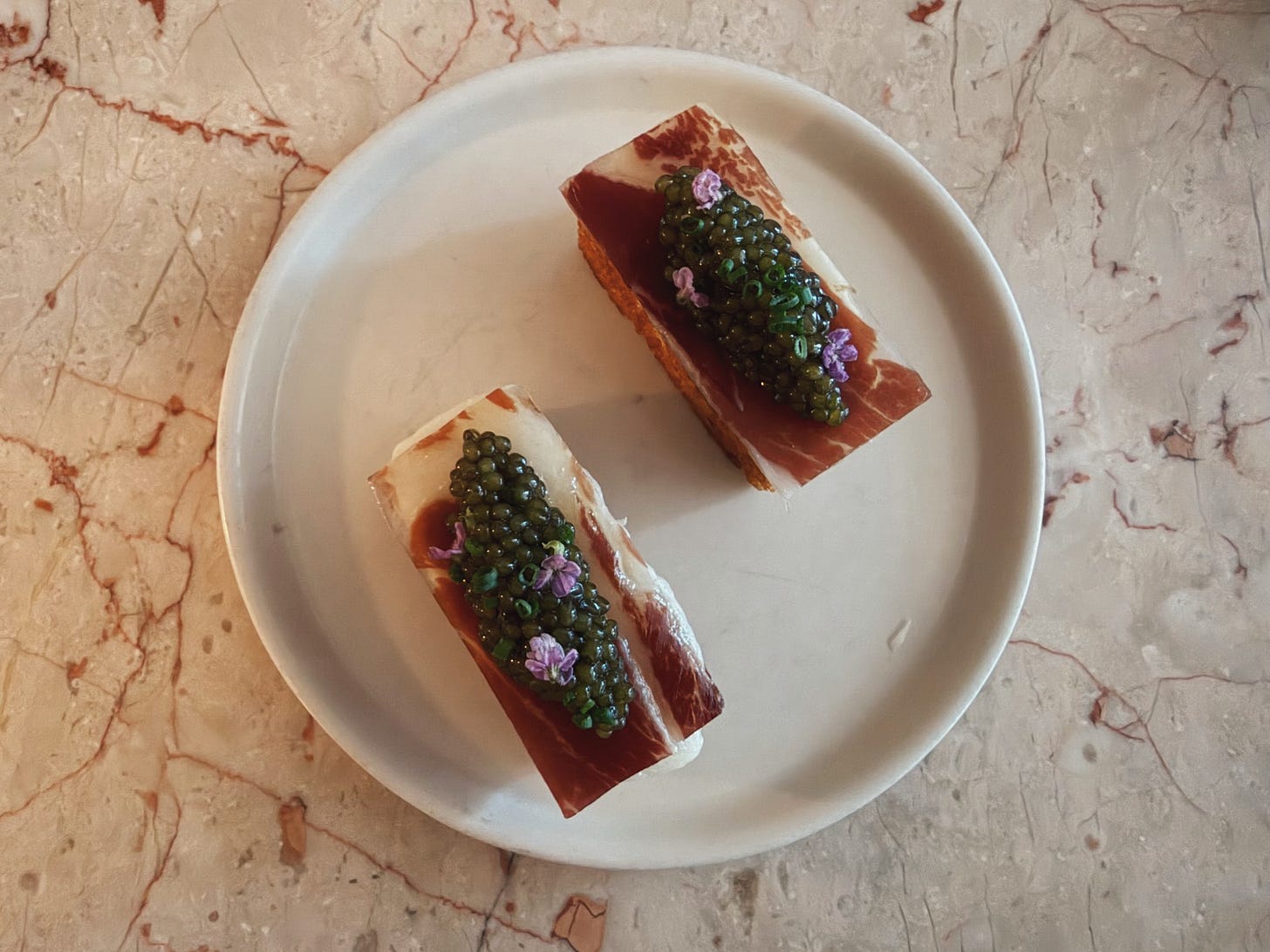Two small Croque Madame bites topped with caviar on a ceramic plate at Jeune et Jolie in Carlsbad.