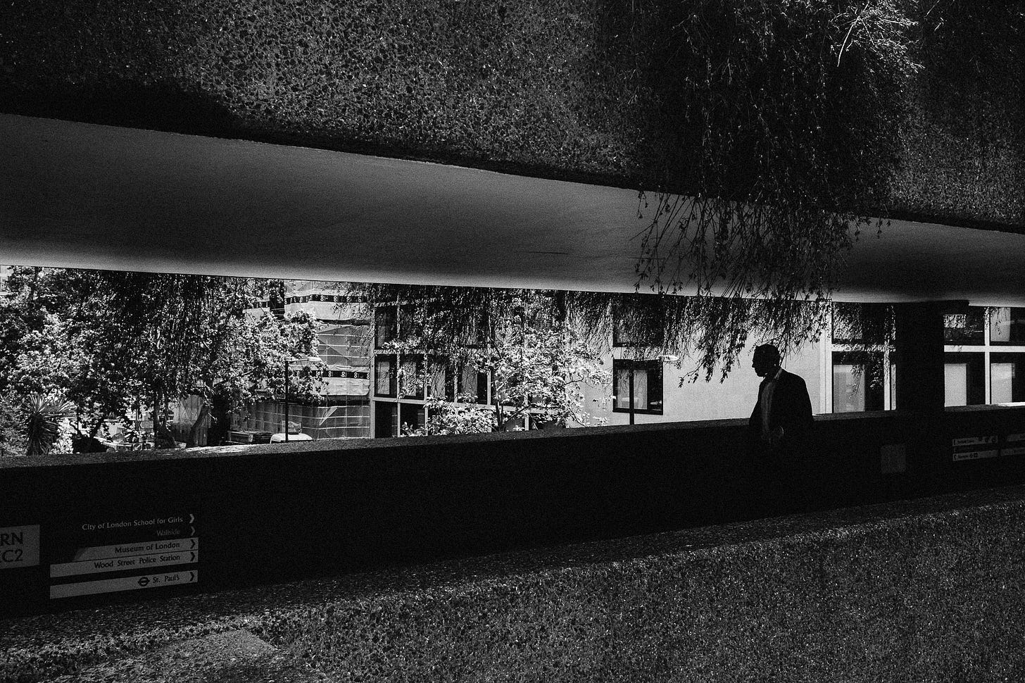 Barbican in London, 2015. A man walks along a corridor inside the Barbican. There are plants hanging all around the corridor.