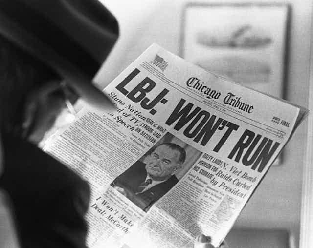 A man is reading a newspaper headline that says LBJ won't run in very large letters. A man is reading a newspaper headline that says LBJ won't run in very large letters.