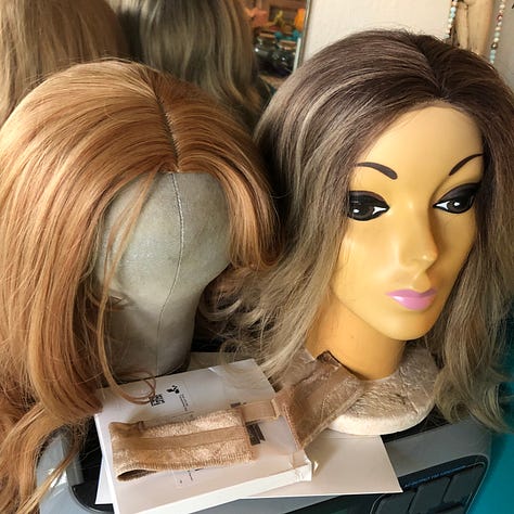 Gallery of sparkly costumes and costuming supplies, two wigs in golden brown on mannequin heads, and gold-leaf leather in a pile on the floor.