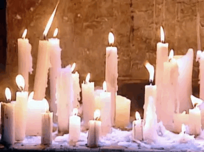 This may contain: many white candles are lit in front of a stone wall with snow on the ground