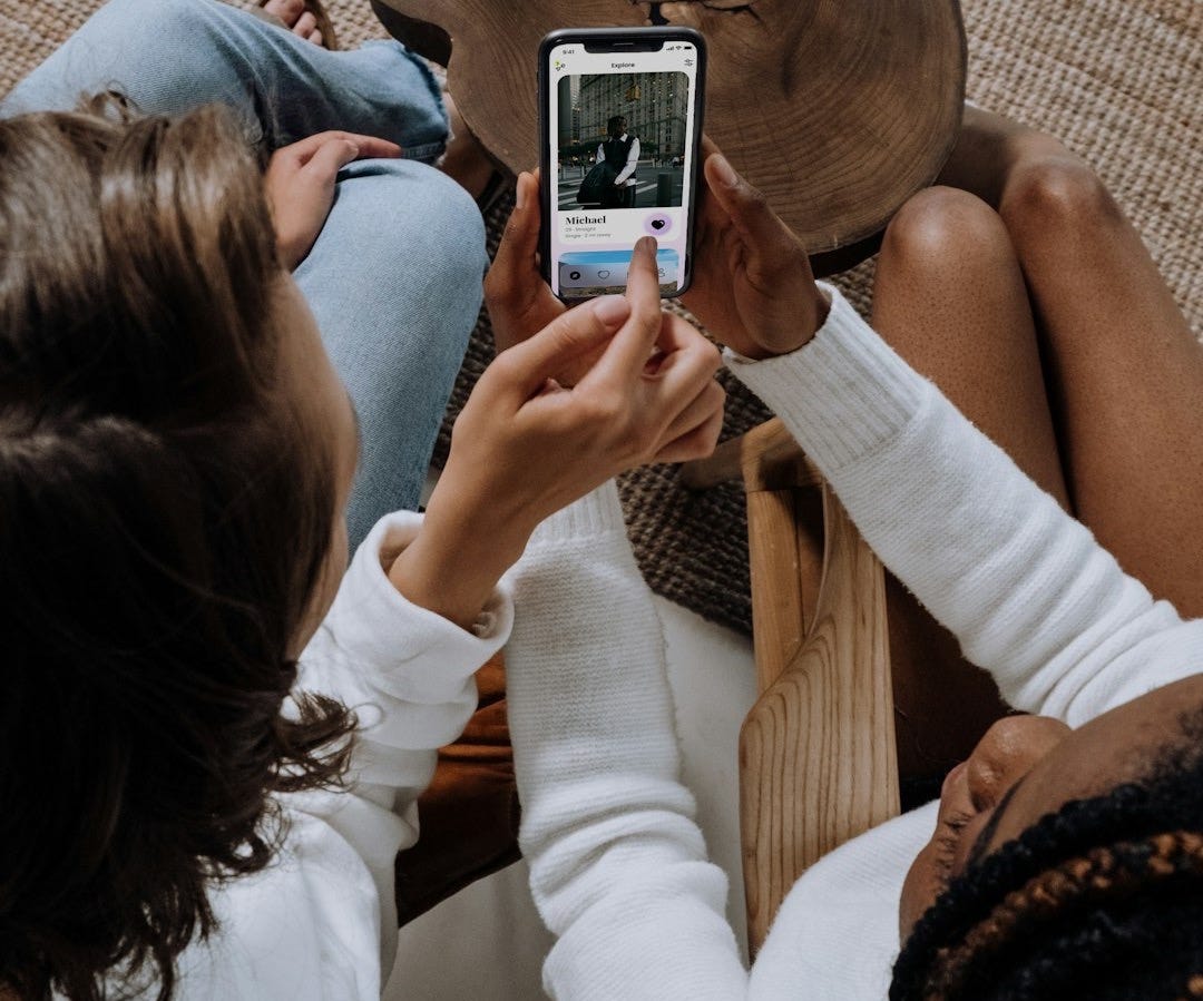 two women sitting on a couch looking at a cell phone