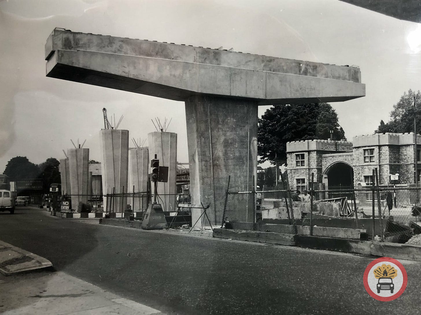Black and white photograph of the M4 viaduct at Brentford under construction. One concrete pillar in the centre of the frame supports a wide T-shaped cross beam; a series of other pillars have also been built in the distance with reinforcement bars sticking out of the top.