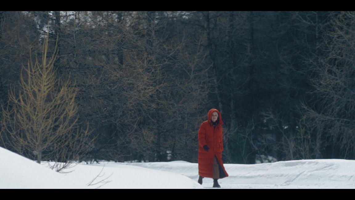 Women in a red coat walking through a forest. Snow on the ground.