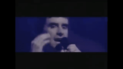 GIF of Chris de Burgh, a white man in a suit with dark hair, singing Lady in Red