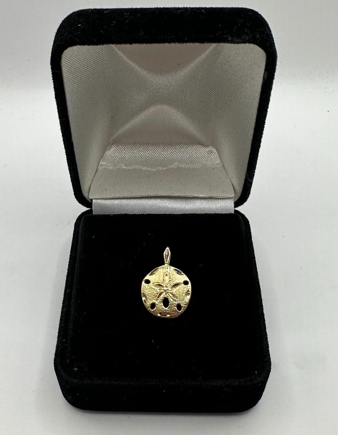 May include: A gold sand dollar pendant charm in a black velvet jewelry box. May include: A gold sand dollar pendant charm in a black velvet jewelry box.