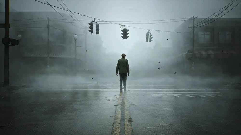 A man stands at an intersection in a small town, the road empty except for the rolling fog