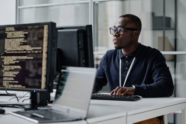 Developer working with new program African American young developer in eyeglasses concentrating on his online work on computer sitting at workplace software engineering  stock pictures, royalty-free photos & images