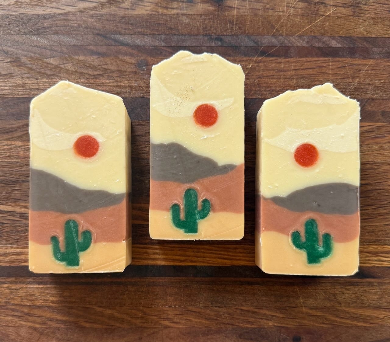 Three handmade soap bars patterned with a simple desert landscape in soft earth tones.