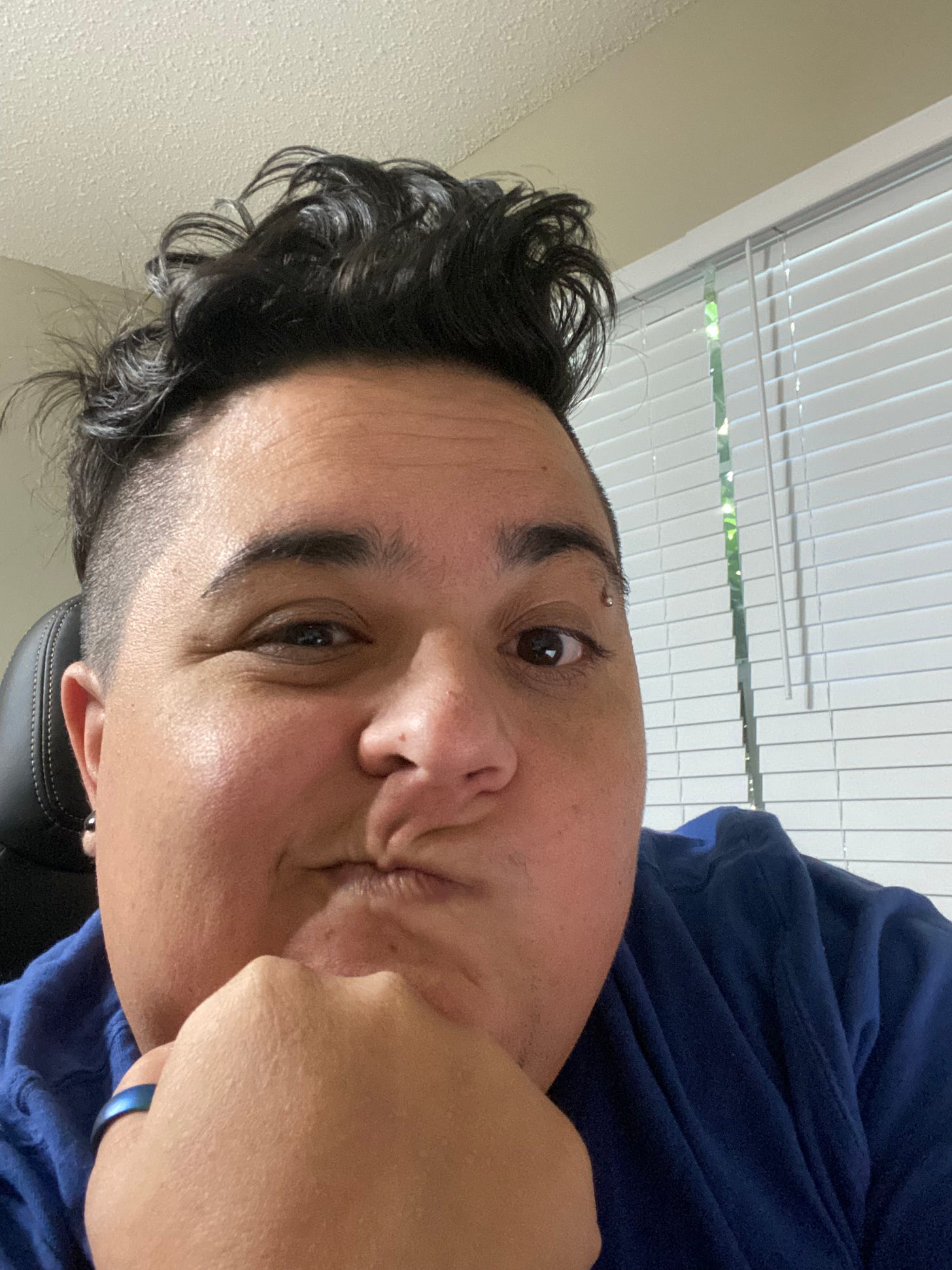 butch boudoir project captain wearing a blue shirt smirking with their hand on their chin