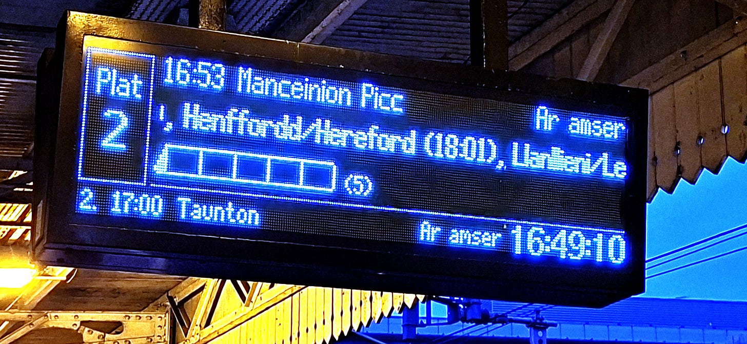 Train sign at station with English town names in Welsh