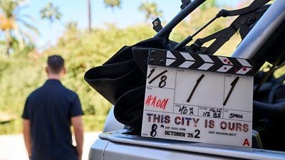 A clapperboard for filming on This City Is Ours series 2 rests on the back of a truck with filming visible in the background A clapperboard for filming on This City Is Ours series 2 rests on the back of a truck with filming visible in the background