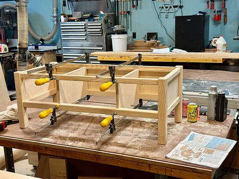 Three-step woodworking process. Left: wooden legs and rails laid out on a table saw for fitting. Center: cutting grooves into rails with a router table. Right: bench frame clamped together on a workbench during glue-up.