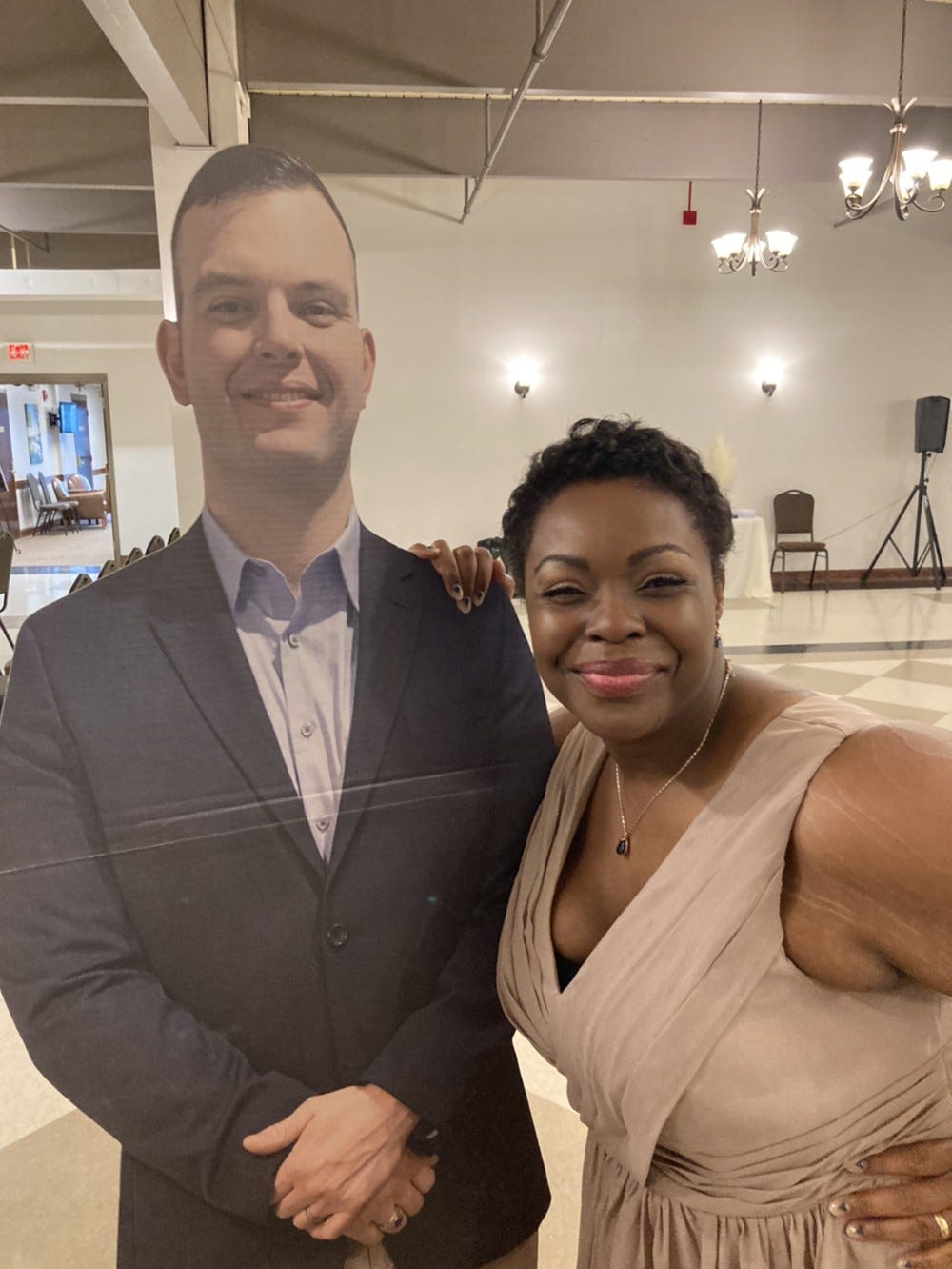 A smiling woman with her arm around a life-size cardboard photo of a smiling man