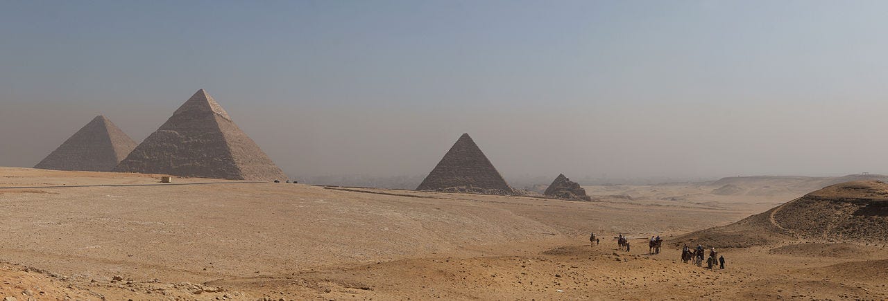 Desert sand, with pyramids in background and human figures to the left