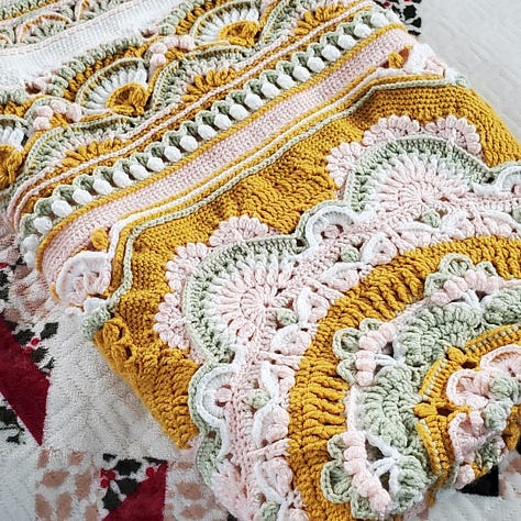 A crocheted mandala afghan blanket in goldenrod, sage, pink, and white.