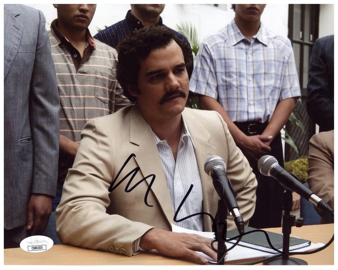 Businessman seated at a press conference table with microphones, surrounded by colleagues.