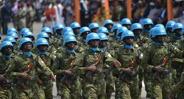 Soldiers wearing UN blue helmets and carrying AK 47s march. 