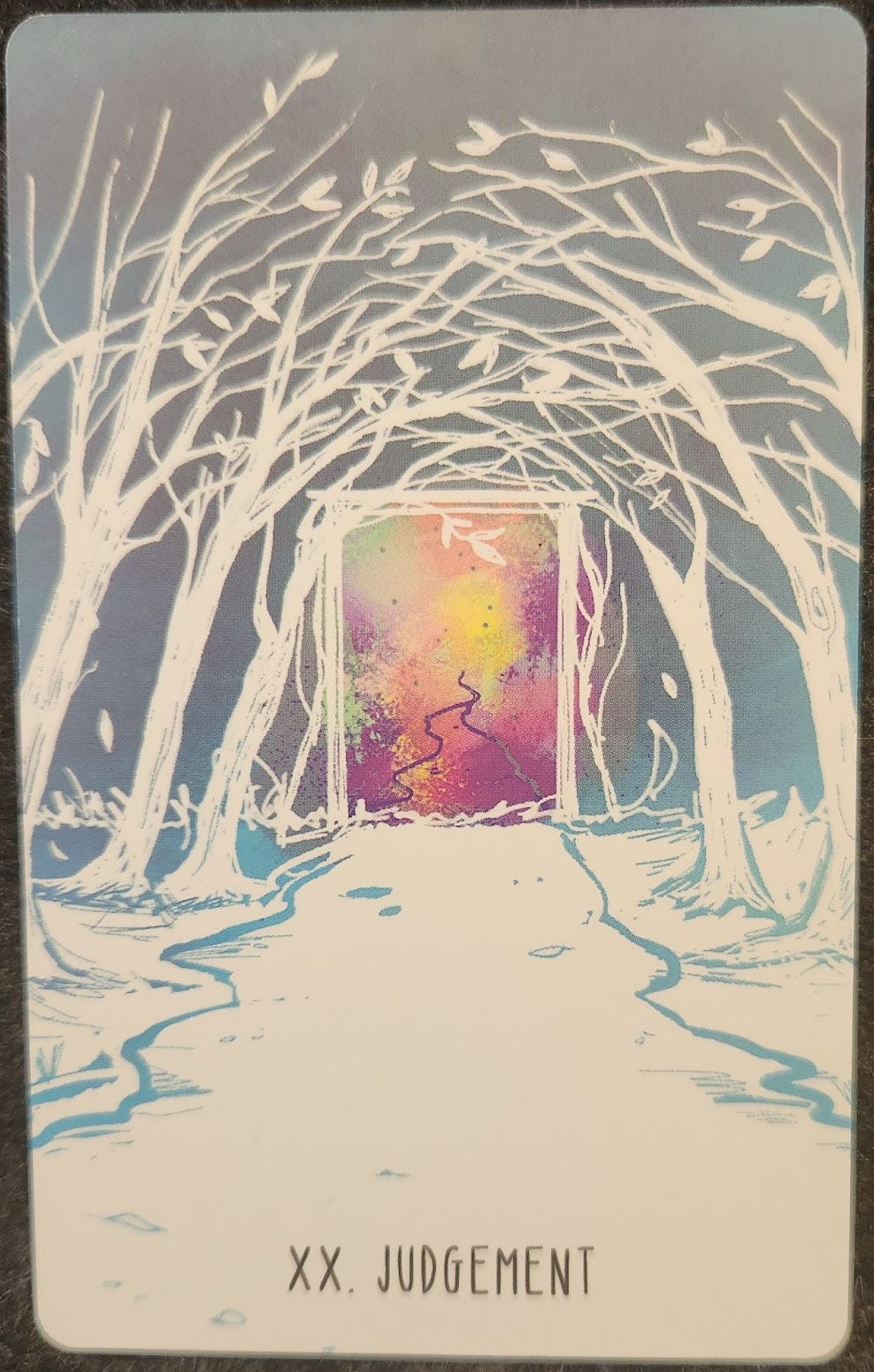 A tarot card labelled XX. Judgement. Path through the woods between two rows of trees. The path and trees are white. At the end of the path is a doorway. The doorway is filled with pink and yellow colours. 