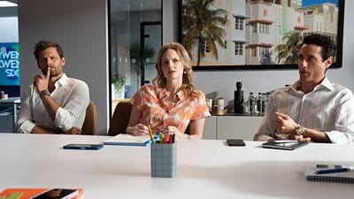 Three Twenty Twenty Six cast members sat at a white table laid with their mobile phones, notebooks and pens. They all look deep in thought.