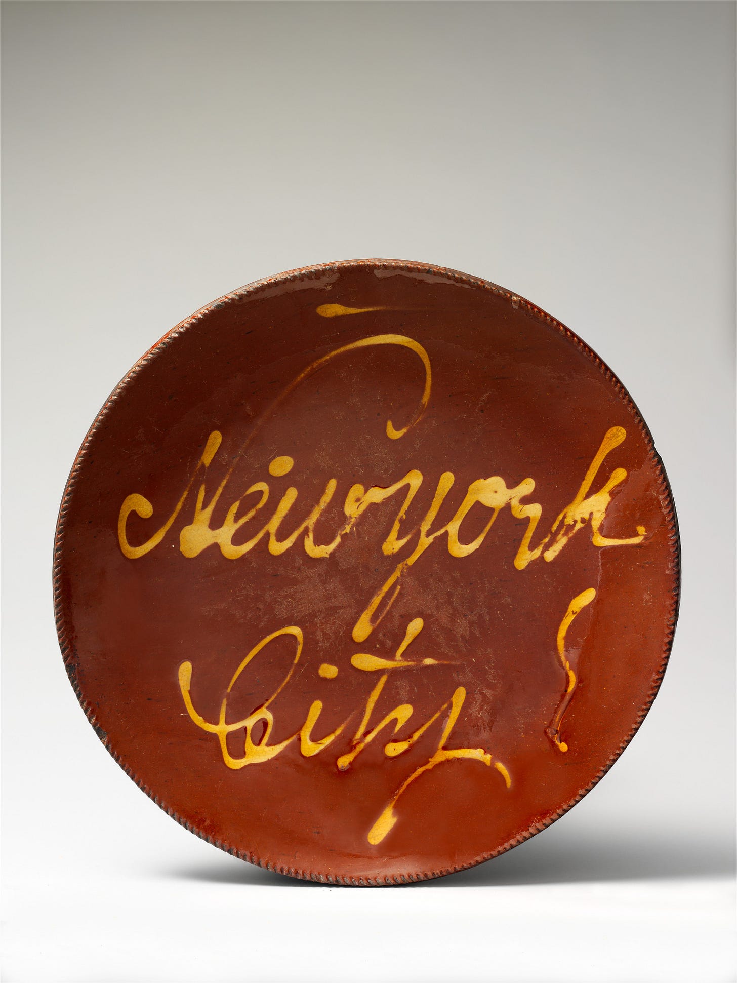red earthenware plate inscribed across the face with the word "New York" in fancy yellow script