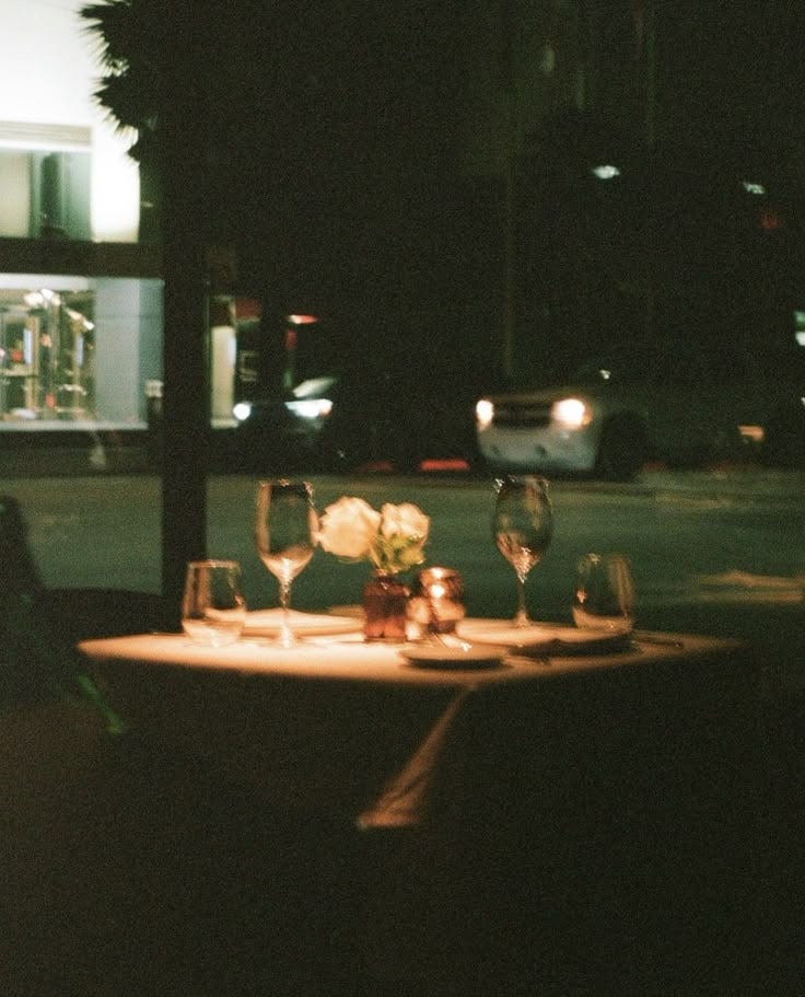 This may contain: a table with wine glasses and flowers on it in the middle of a street at night This may contain: a table with wine glasses and flowers on it in the middle of a street at night