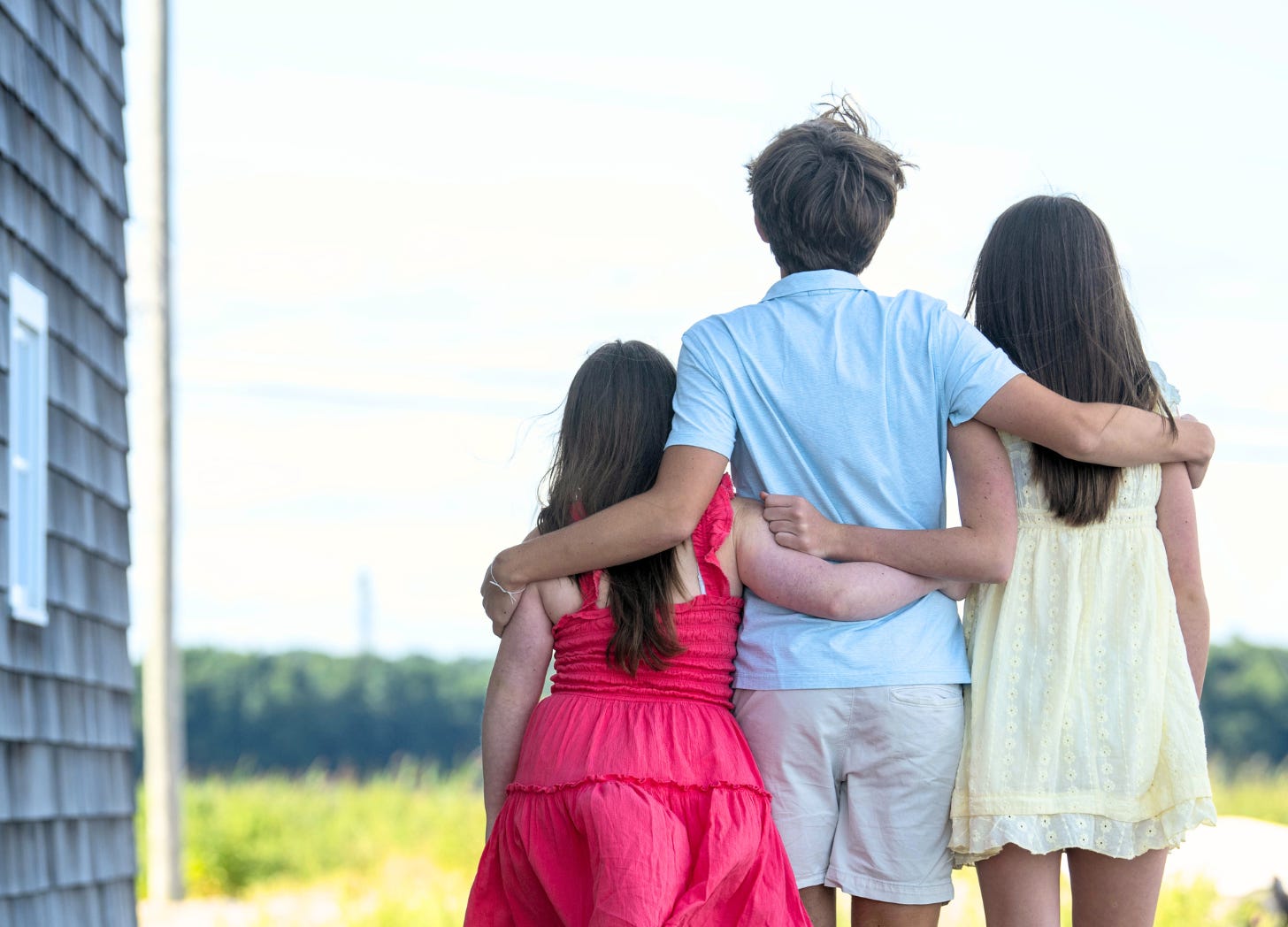 Penny, William, and Marilee outside on a sunny day walking away from the camera with their arms around each other.