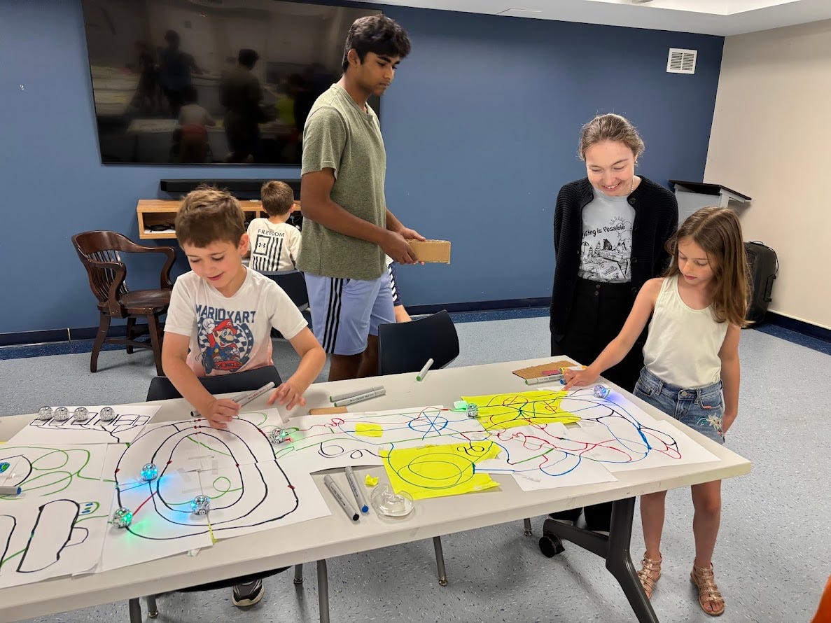 Two kids racing their Ozobots across two tables of colorful mazes.