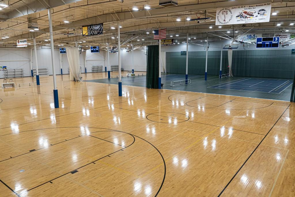 Photo of a large, indoor gymnasium. In view are 6 half-size basketball courts. It is implied that more space is outside of the image.
