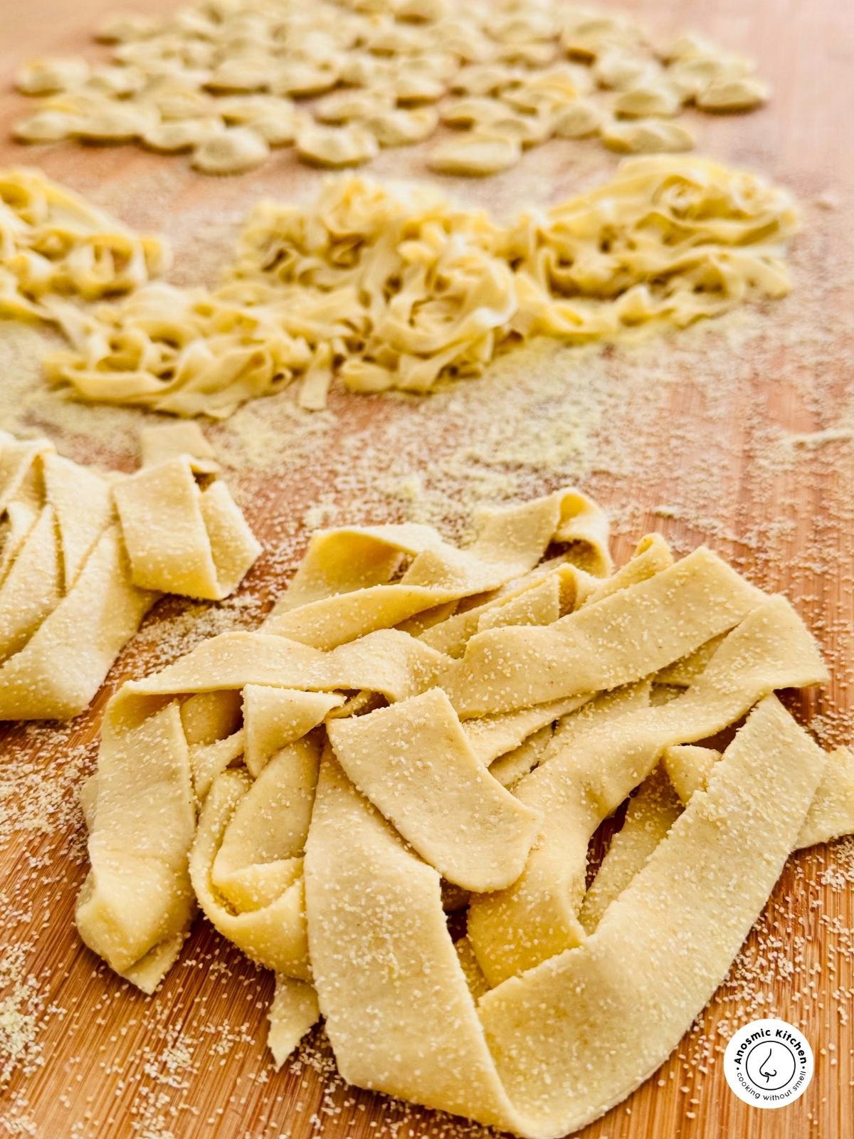 Freshly rolled homemade pasta, including orecchiette, fettuccine, and pappardelle, dusted with semolina on a wooden surface.