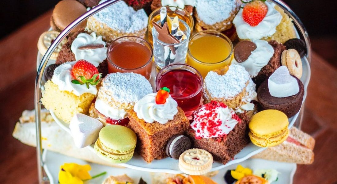 An afternoon tea platter with cakes, biscuits, macarons, and juice glasses on it An afternoon tea platter with cakes, biscuits, macarons, and juice glasses on it