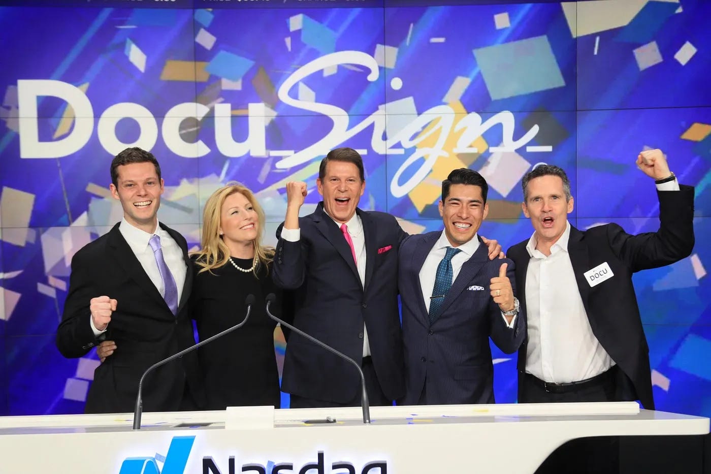 DocuSign executive team celebrating the company's April 2018 Nasdaq IPO with confetti on the Nasdaq trading floor, marking the public listing of the $9 billion electronic signature company that built its entire business model on charging $10 to $65 per user per month for putting names on PDFs, with Personal plans at $10 to $15 per month, Standard plans at $25 to $45 per user per month, and Business Pro plans at $40 to $65 per user per month, plus add-ons including $0.40 per SMS delivery, $2.50 per ID verification, and 100-envelope annual caps that force a 50-person team to pay $24,000 to $39,000 per year for digital signatures.
