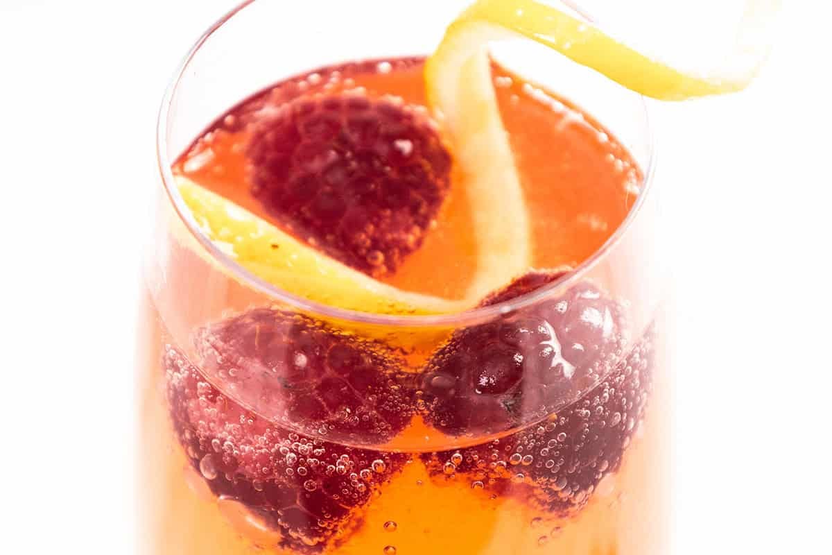 Raspberry blush Prosecco cocktail with fresh raspberries and lemon slices in a glass.
