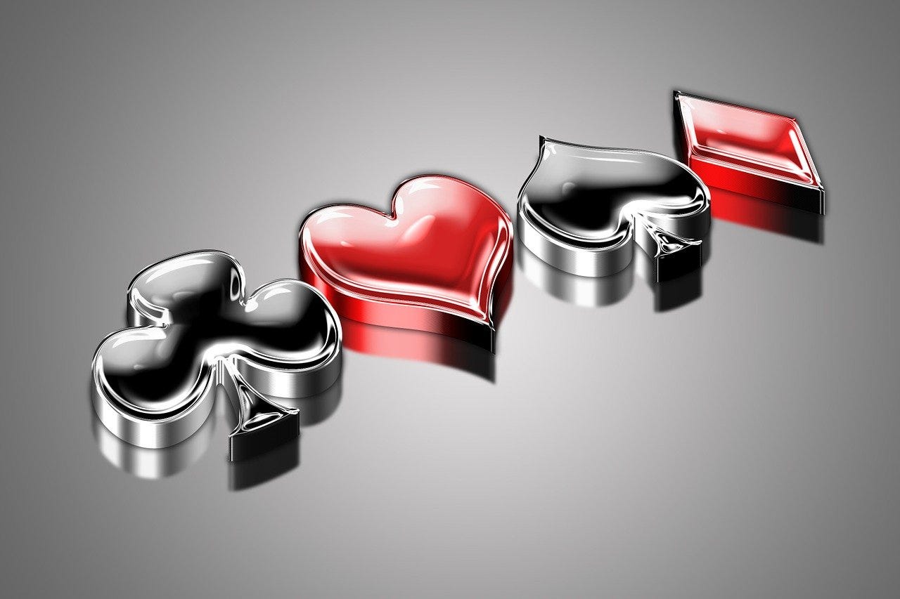 Glossy 3D render of four playing card suits—club, heart, spade, and diamond—set against a reflective grey surface. Glossy 3D render of four playing card suits—club, heart, spade, and diamond—set against a reflective grey surface.