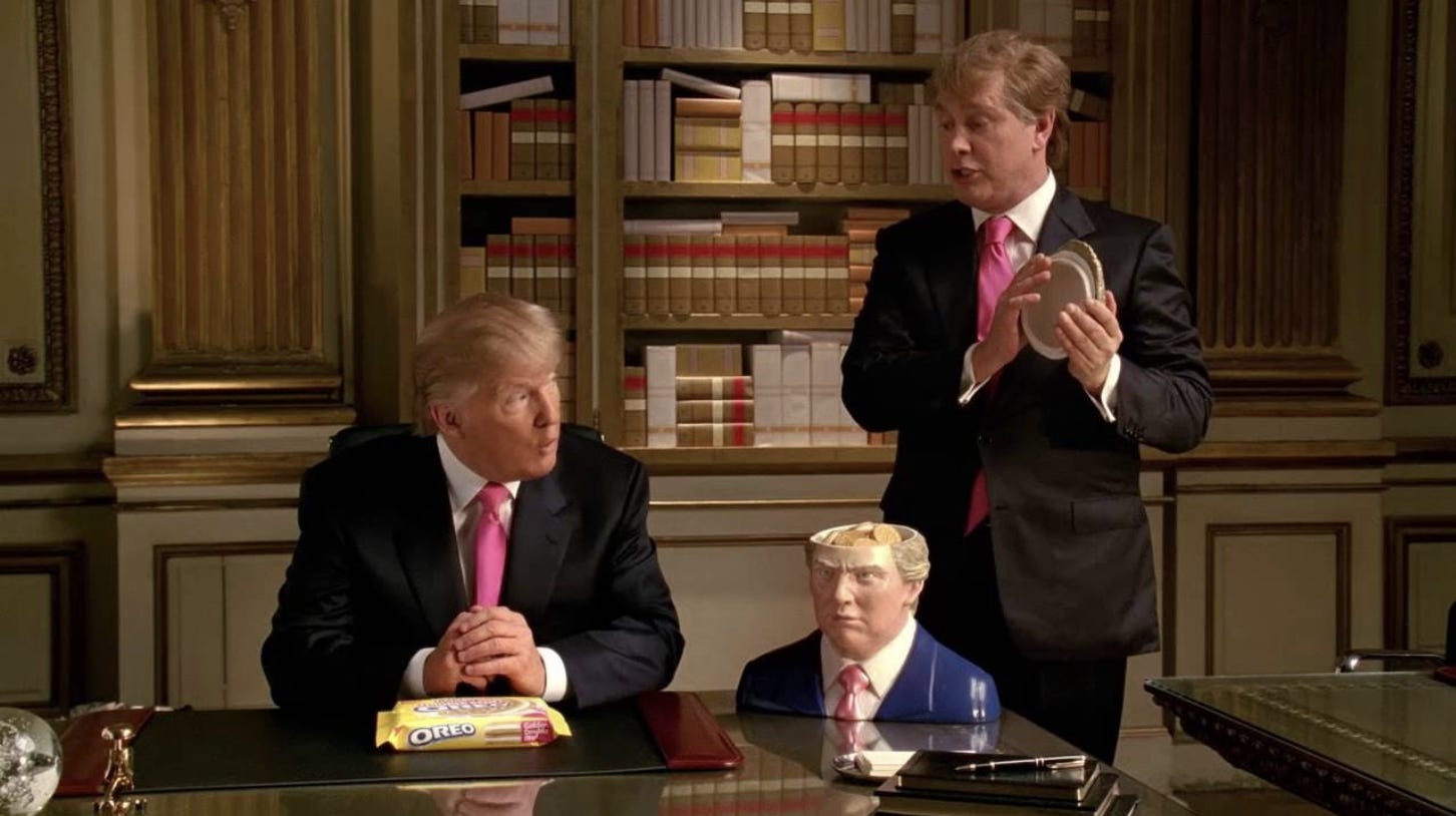 Trump sits at his desk with a Trump-shaped cookie jar and a Trump impersonator standing next to him.