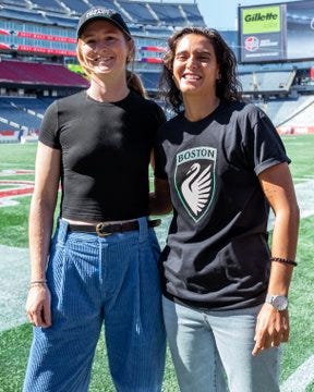 Sam Mewis and Filipa Patão standing on a soccer field, smiling. Sam wears a black cap, black shirt, and blue pants, while Filipa wears a black shirt with a Boston Legacy FC logo and blue jeans. Both are in a stadium with green field and blue seats visible. A group photo shows Sam Mewis, Filipa Patão, and others, including a man holding a baby, all wearing Boston Legacy FC shirts, standing in front of a backdrop with the Boston Legacy FC logo. Another image shows Sam Mewis and Filipa Patão talking on the field, with stadium seating in the background.