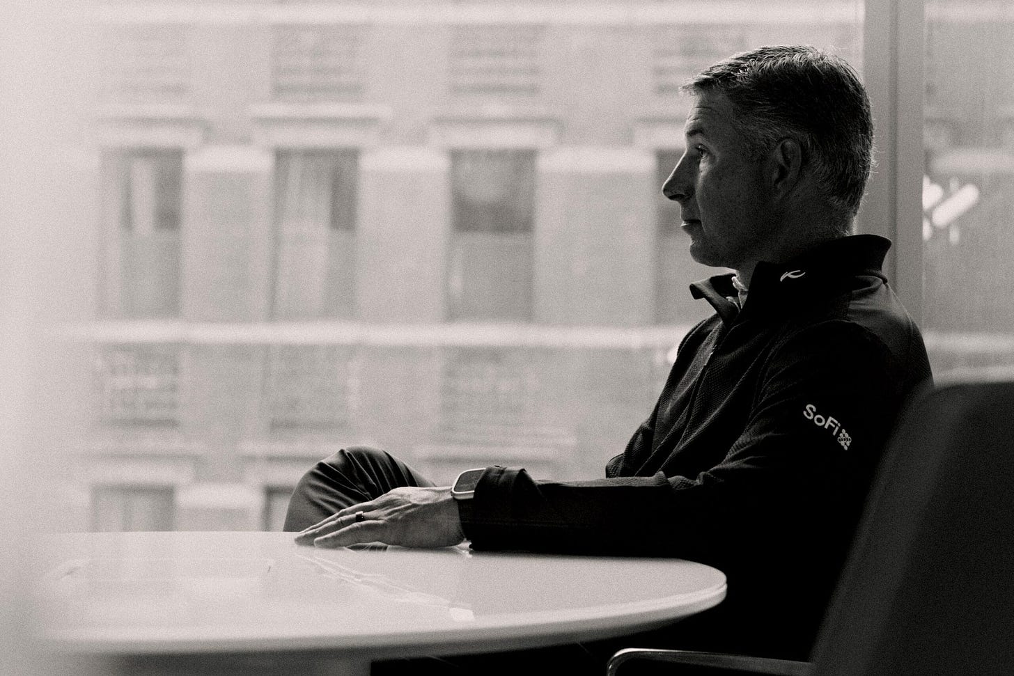 Portrait of Social Finance CEO Anthony Noto seated facing the left and wearing a quarter-zip shirt with the SoFi logo on the left arm.