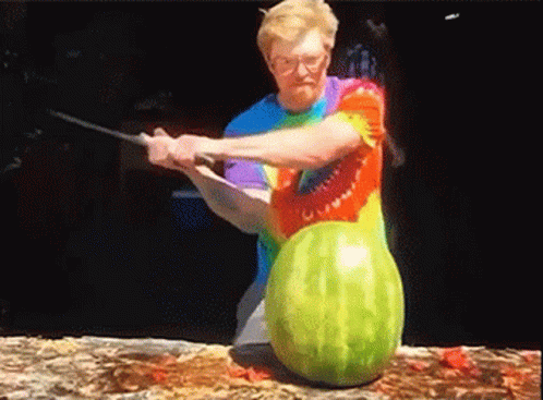 Dude in tie-dyed t-shirt slashes through a watermelon with a samurai sword.