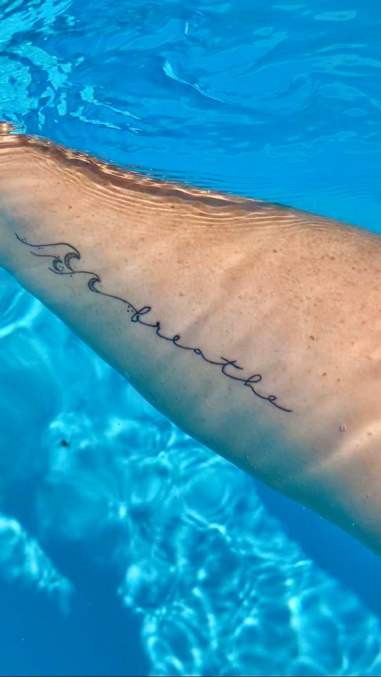 picture of melissas tattoo on her forearm that reads "breath"