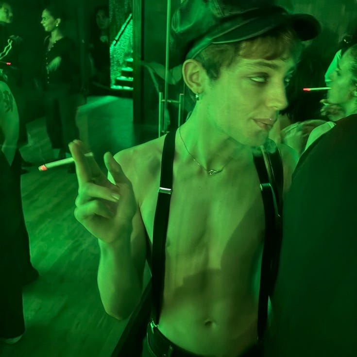 A person in suspenders and hat smoking a cigarette

Description automatically generated