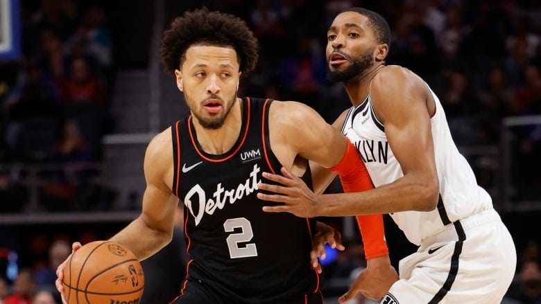 A basketball player wearing black uniform protects the ball from an opposition player wearing white. A basketball player wearing black uniform protects the ball from an opposition player wearing white.