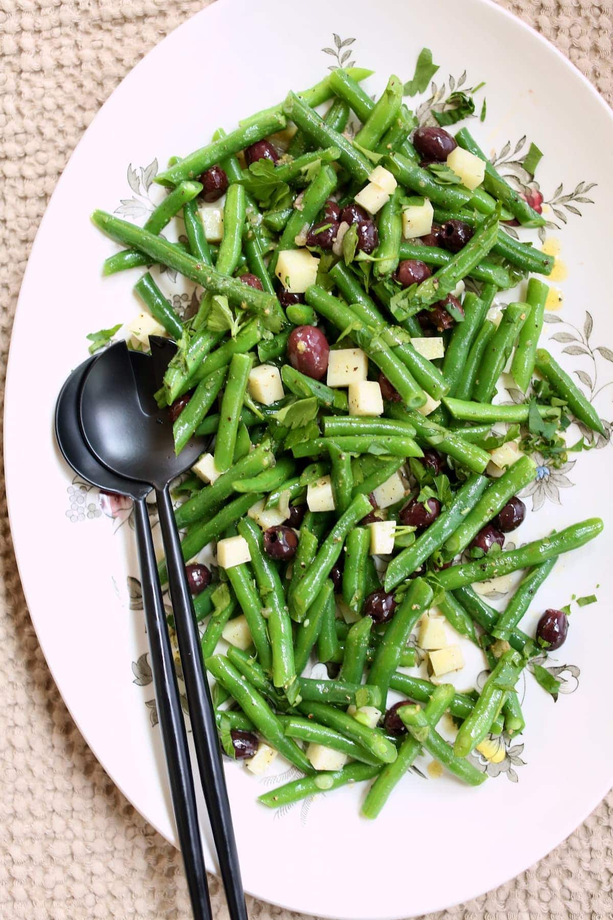 a large platter with green bean salad on it and black utinsils.  