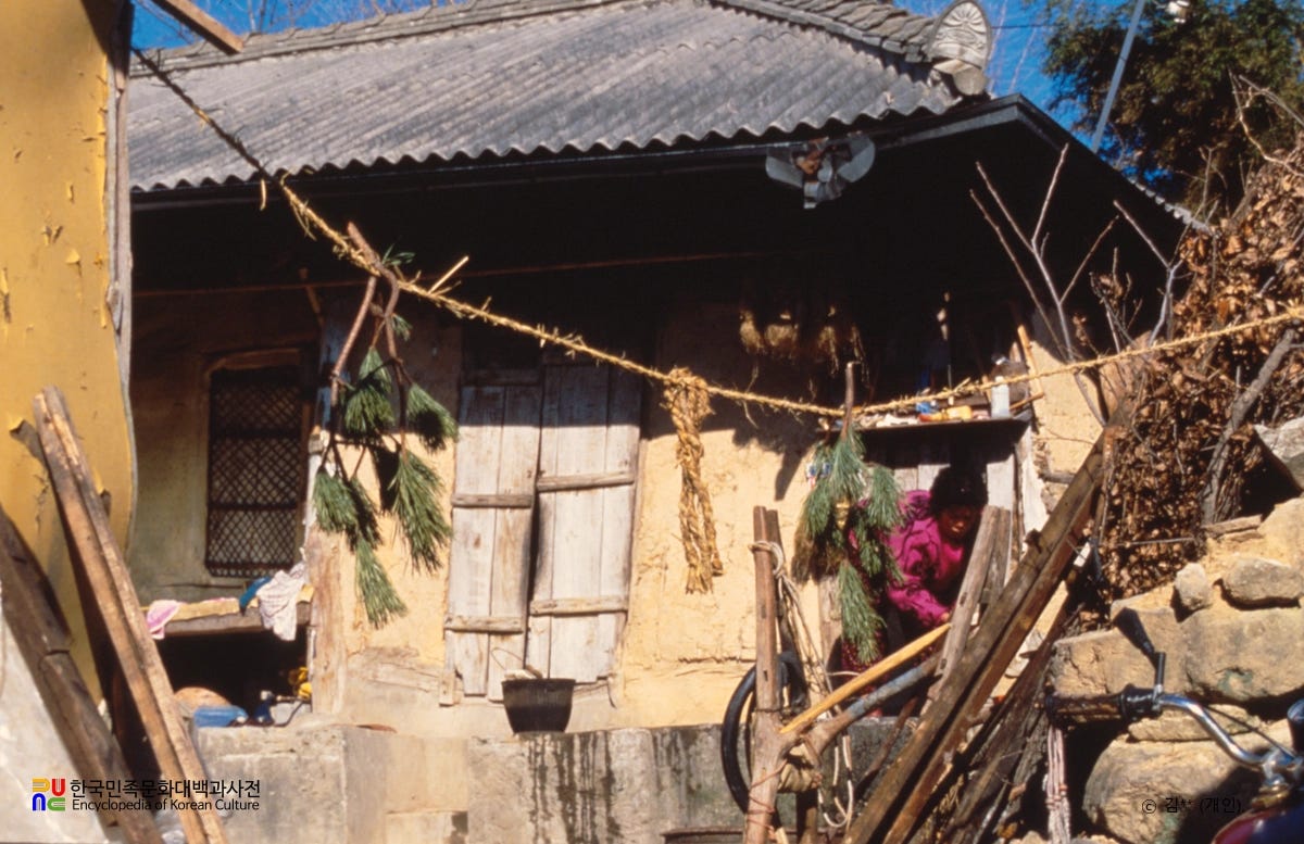 A traditional Korean house with a geumjul, or sacred straw rope, hanging across the entrance. The rope is decorated with pine branches, marking the home as one where a baby has recently been born and the household is in a protected postpartum period.