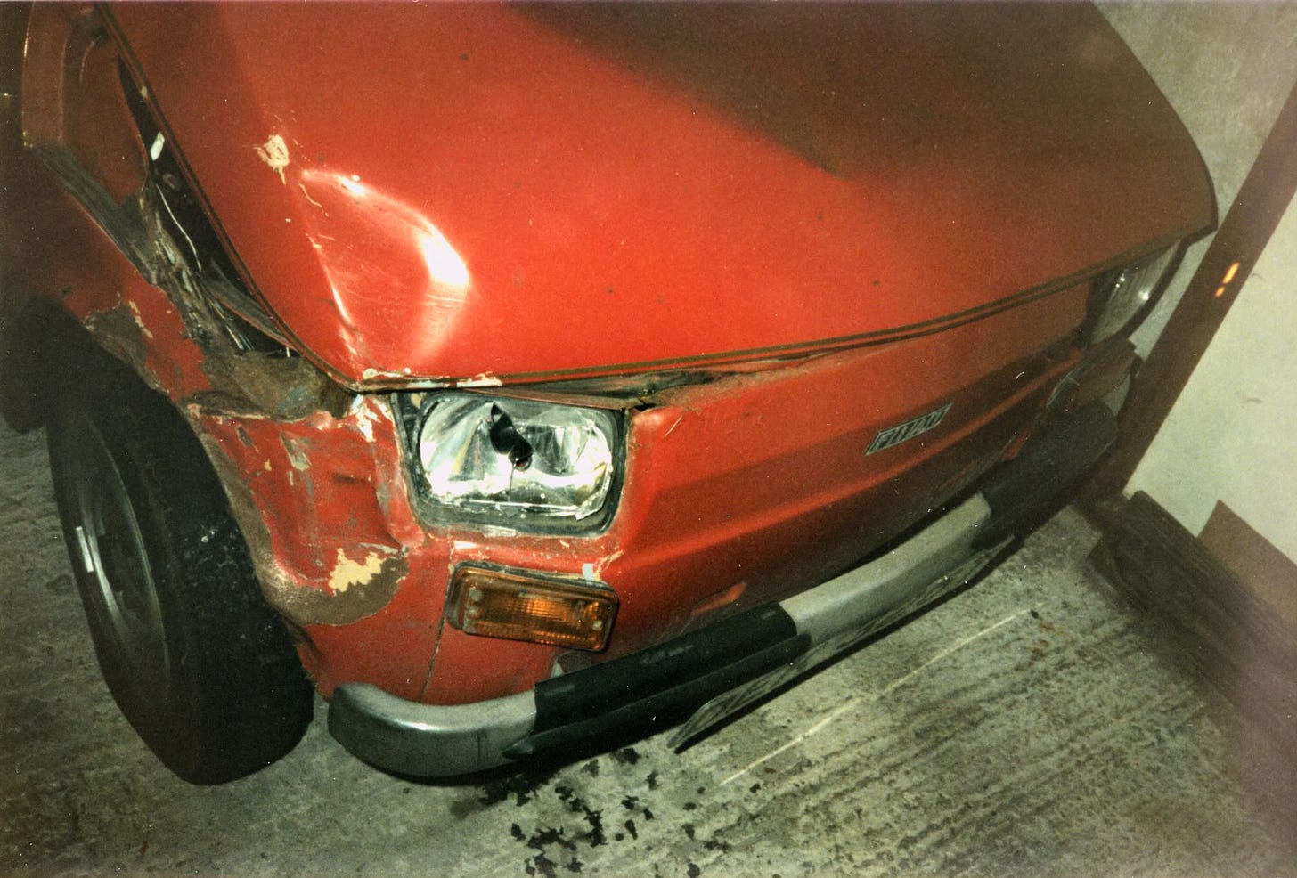 The front of a 1979 accident-damaged red Fiat 126. 