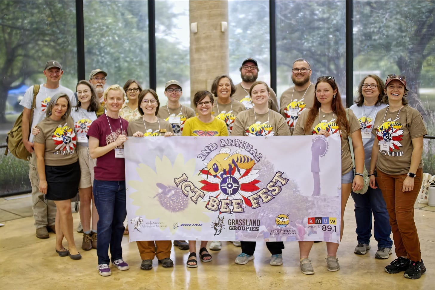 Bee Fest volunteers stand together behind a large banner displaying the Bee Fest logo and sponsors.