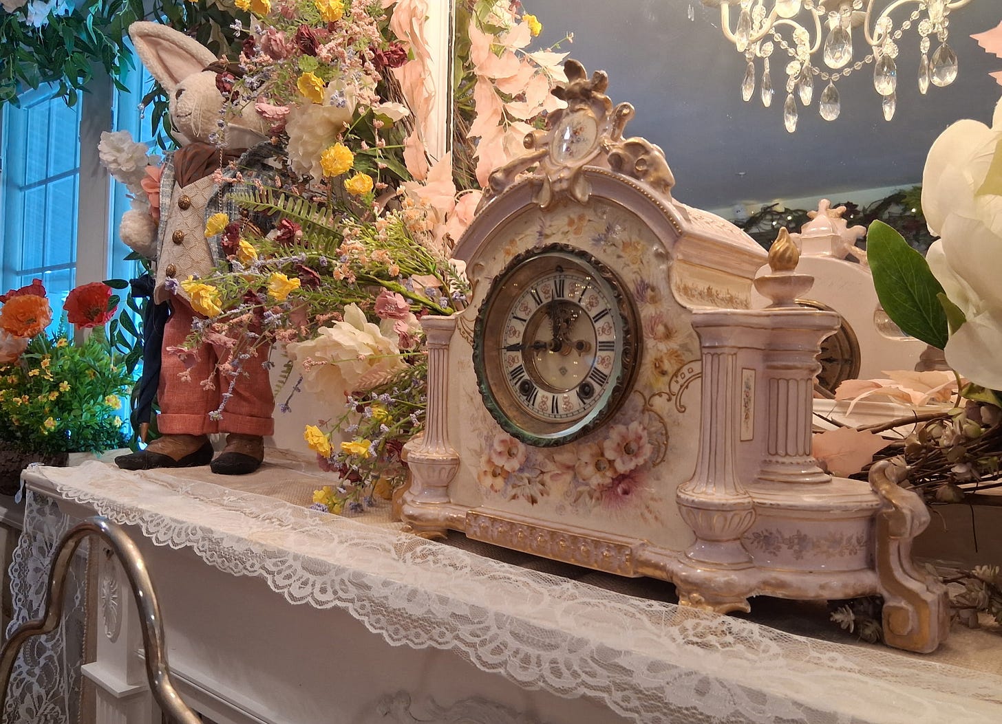 Photo of an ornate antique clock on a Victorian style fireplace mantel with flowers and a white rabbit figurine.