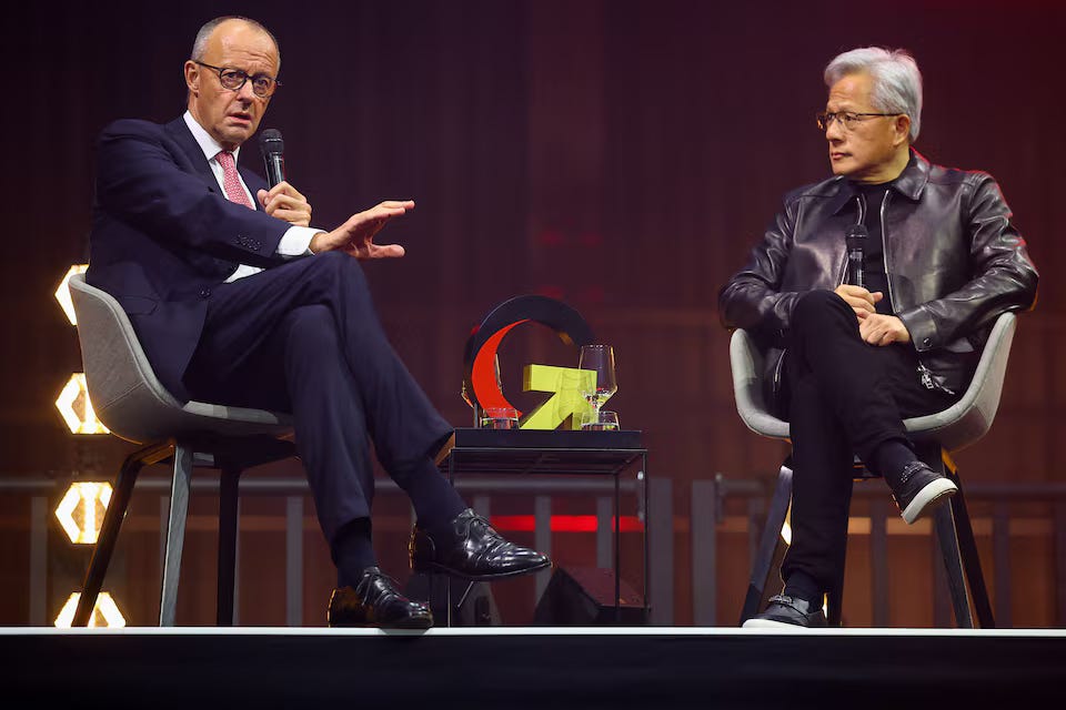 Two men in conversation on stage, one holding a microphone, at an event on AI and Nvidia in Germany Two men in conversation on stage, one holding a microphone, at an event on AI and Nvidia in Germany