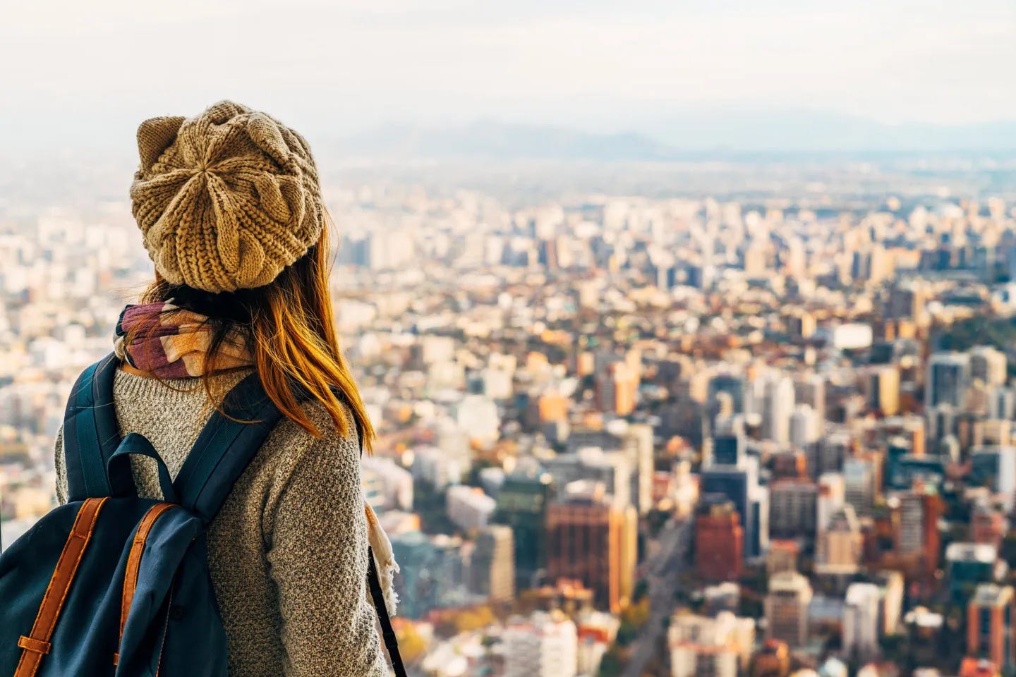 a female solo travaler standing on a big hill, looking down at a large city and wondering if it is a safe place for women