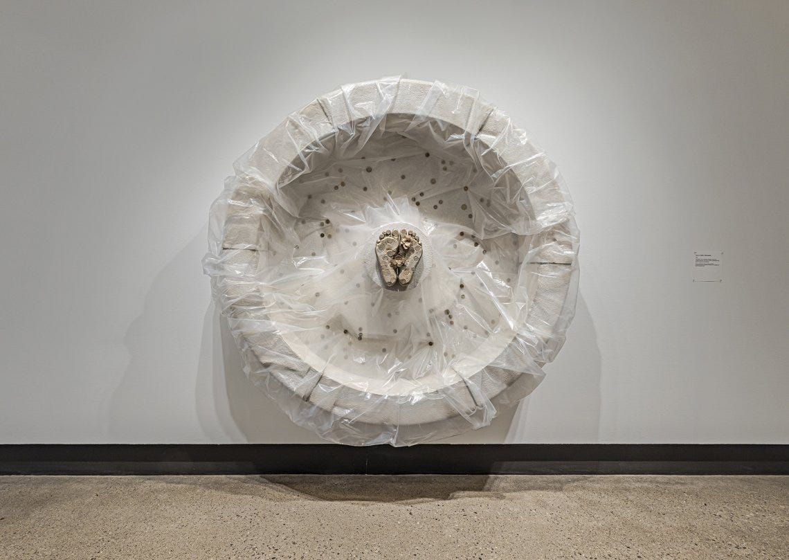 Concrete sculpture wrapped in plastic with a casting of feet emerging from the centre