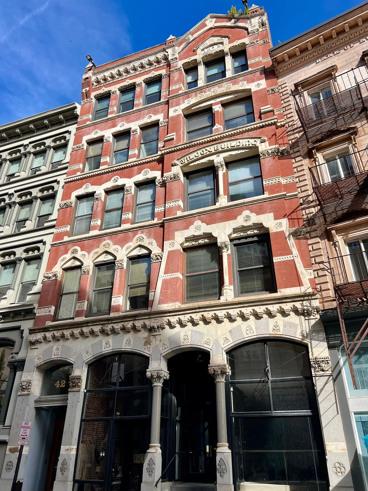 Historic Wilcox Building in downtown Providence, Rhode Island, featuring ornate red brick and white stone facade with arched windows, decorative cornices, and intricate architectural details under a clear blue sky — a classic example of late 19th-century urban design.